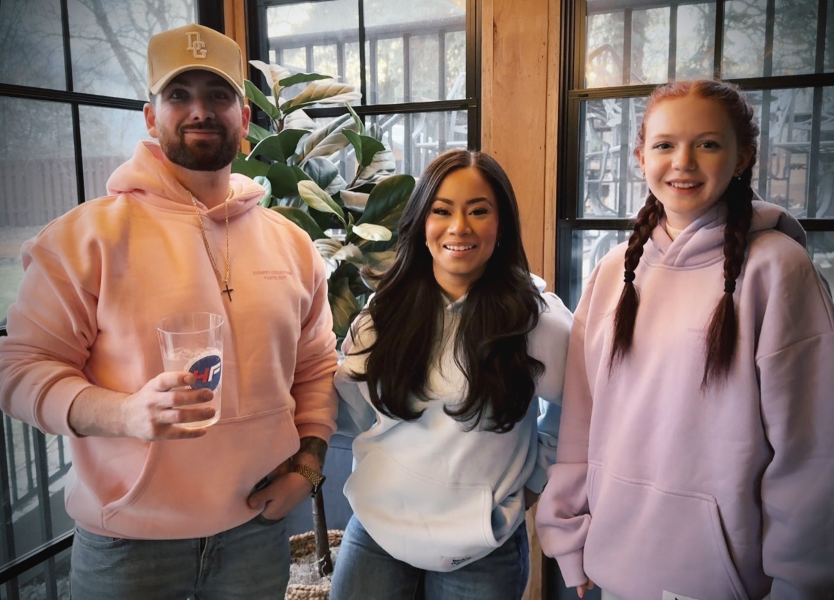 Three people standing together, each wearing a different color of the hoodie.